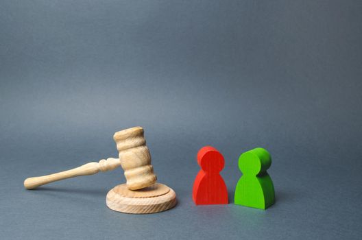 Two figures of people opponents stand near the judge's gavel. The judicial system. Conflict resolution in court, claimant and respondent. Court case, settling disputes. Legal advice, lawyer services.