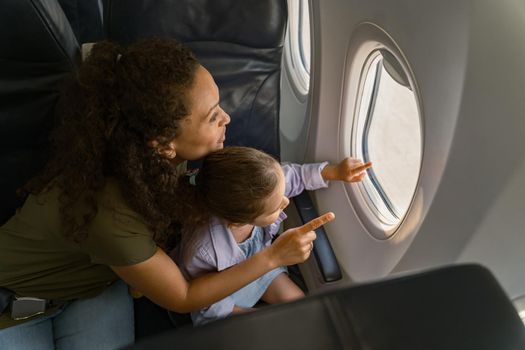 Top view of smiling woman with kid sitting together on a plane and looking out the window