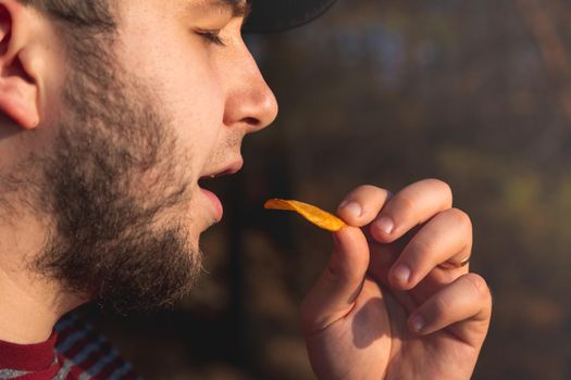 Bearder Man in forest eating chips. In park image outdoors with blurred background.