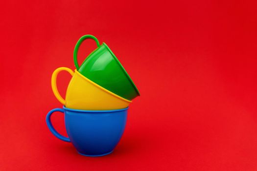 Tree cups of different colors one in another on red background. Mugs are green, yellow and blue. Enough space for text.
