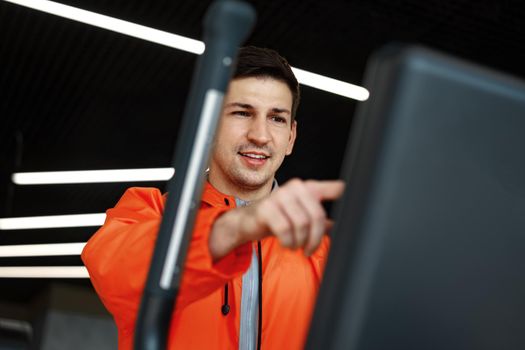 Portrait of a young man in orange windbreaker workout on a fitness machine at a gym.