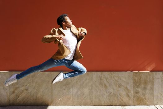 Young black man doing an acrobatic jump on red urban wall. Cuban guy.