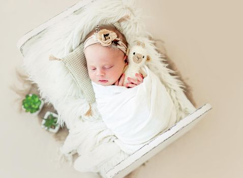 Sleeping newborn baby girl wrapped in white blanket in a small crib