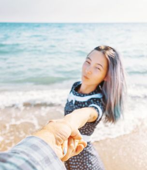 Young woman holding man's hand and leading him to sea, point of view. Focus on hand.