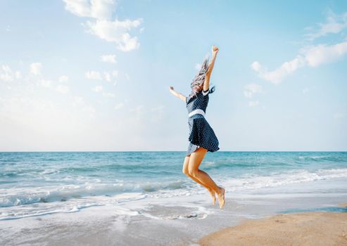 Happy young woman jumping on sand beach near the sea on vacations.