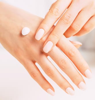 Young female hands with manicure of beige natural color applying moisturizing cream, concept of skincare and beauty.