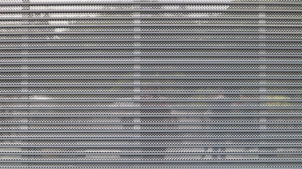 Close-up of a gray metal mesh as a security measure in front of a closed shopping center. Closed gates at the entrance to the store that impede the entry or destruction of places for criminals