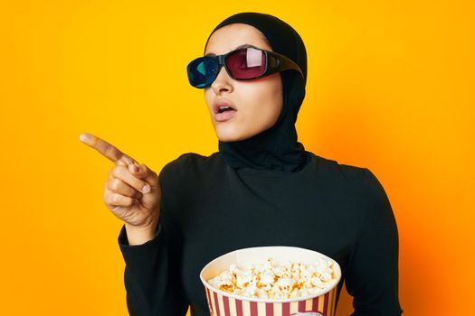 arab woman in black hijab popcorn 3D glasses cinema yellow background. High quality photo