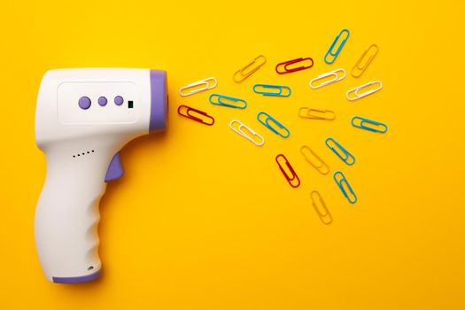 Non-contact infrared thermometer on yellow background with paper clips. Concept of new schooling guidance after coronavirus lockdown