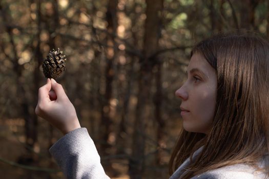 Close up of woman hand holding a pine cone with a natural blurred background. Little girl holds cone in her hands