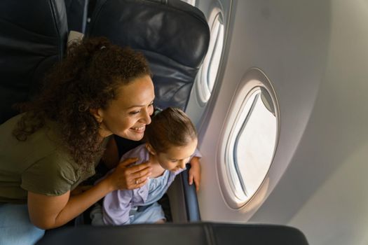 Top view of happy lady and cute girl sitting together on a airplane and looking out the window