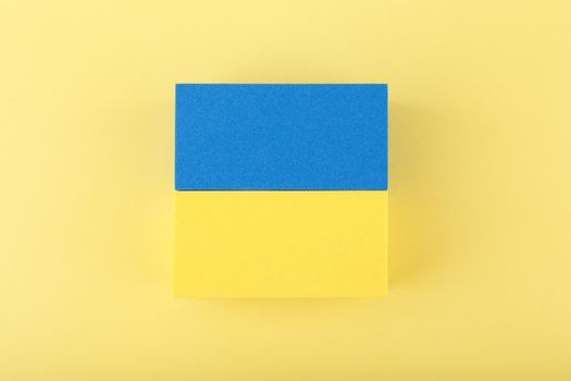 Creative flat lay with national flag of Ukraine made of toy rectangles on bright yellow background. Close up, horizontal, no people.