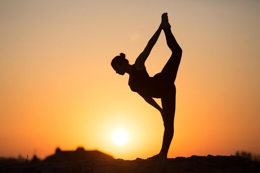 Silhouette of woman doing yoga over orange sun