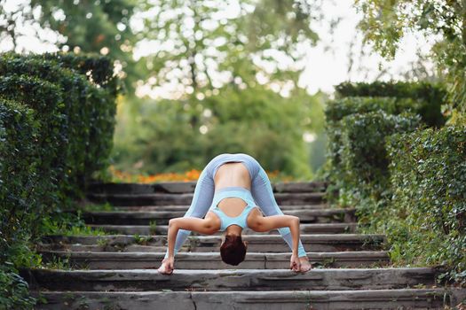 Pretty smiling young sexy woman doing yoga exercises in the park on the stairs