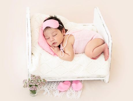 Charming newborn with pink sleep mask lying on tiny bed