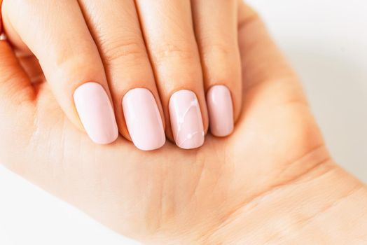 Woman’s hand with manicure of pink pastel color and art design, close-up.