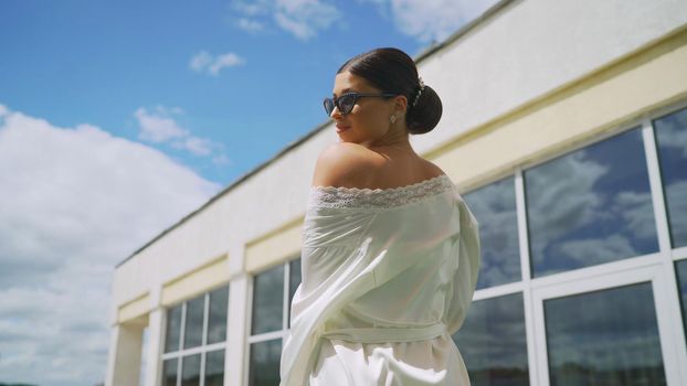Young brunette in a light robe and sunglasses. Girl in a white robe on the roof of the hotel.