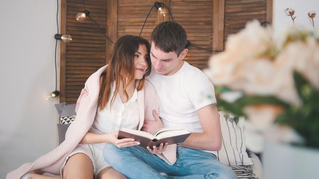 Young man and woman relaxing at home - reading the book on sofa kissing each other happy, close up