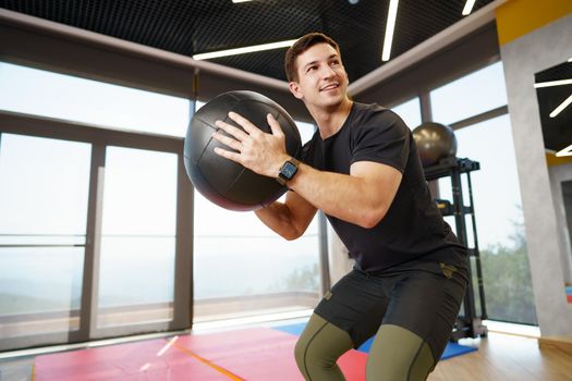 Fit young man exercising with fitness ball in a gym, close up