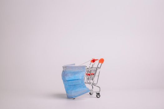 Safe and online shopping on quarantine concept. Shopping cart with protective medical mask against coronavirus. White background, copy space.