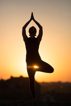 Silhouette of woman doing yoga over orange sun