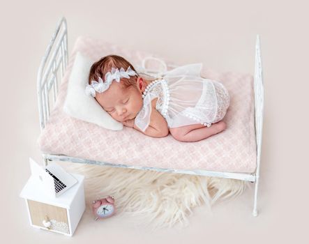 Cute asleep newborn on tiny bed with a laptop on the nightstand