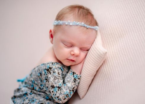 Newborn girl wearing diadem and dress resting on tiny pillow