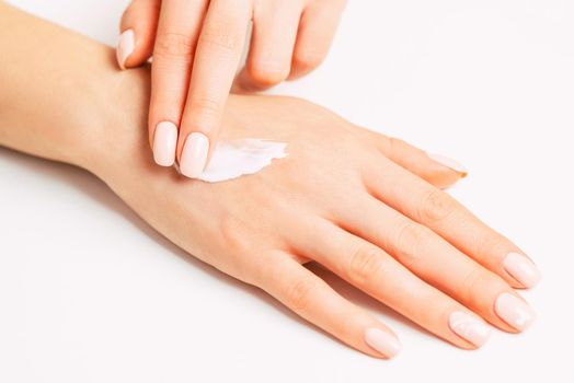 Woman’s hands with beautiful manicure applying moisturizing skincare cream.