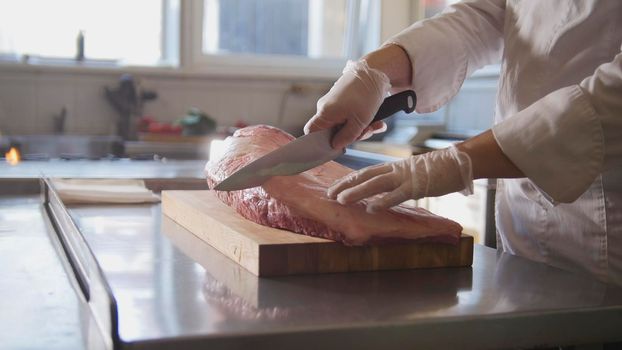 Butcher cutting large piece of fresh raw meat lying on a wooden board in a commercial kitchen, cooking and Haute cuisine concept