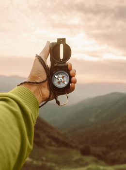 Male traveler explorer searching direction with compass in summer mountains, point of view.