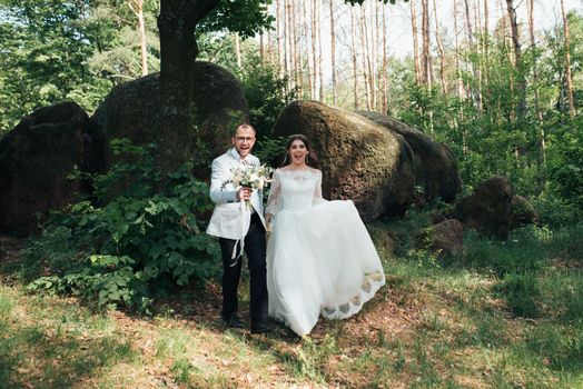 Bride and groom on wedding day, hugging, standing near a rock or a large stone.