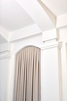 From below of house interior details with white walls and columns and beige curtains