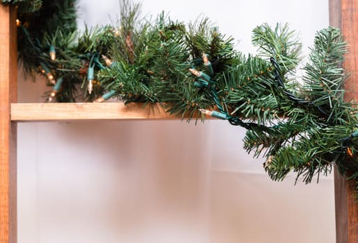 A wooden staircase is decorated with a garland of a Christmas tree and lights. Close-up. Copy space.