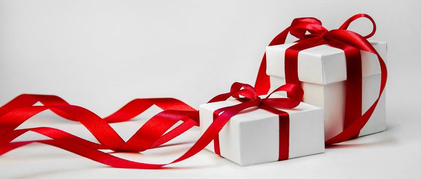Christmas Gift in White Box with Red Ribbon on Light Background. New Year Holiday Composition. Copy Space For Your Text