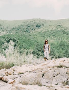 Traveler backpacker young woman walking in summer mountains on rocky terrain.