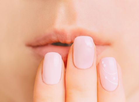 Female hand with pastel pink manicure near lips, close-up. Concept of natural beauty.