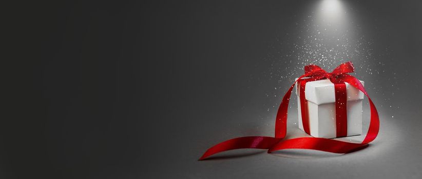 Christmas Gift in White Box with Red Ribbon on Dark Grey Background. Concept. Night Illuminated By The Lantern. Snowing. New Year Holiday Composition. Banner. Copy Space For Your Text