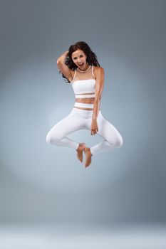 Attractive excited fitness girl in sportwear jumping of joy isolated over light background