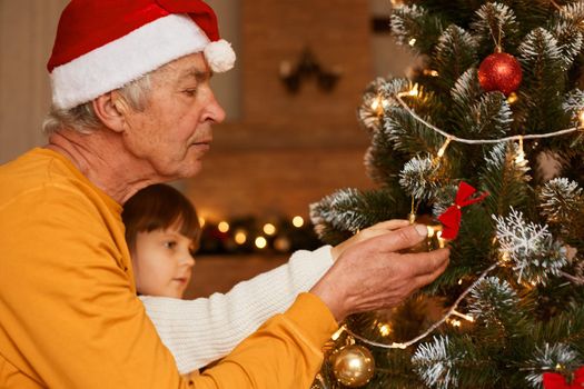 Grandfather and granddaughter in festive room decorating fir tree, little female kid with mature man celebrating new year eve together, merry christmas.
