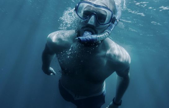 Active young man freediver in mask with snorkel swimming underwater.