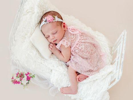 Sleeping newborn baby girl in a pink dress in a small crib