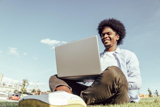 African american young man using laptop in park joyfully