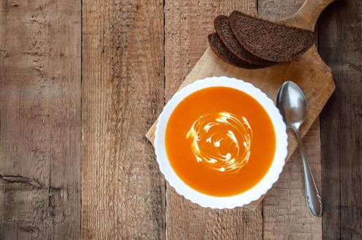 Pumpkin Cream Soup in White Bowl with Bread on Rustic Wooden Background. Autumn Vegetarian Food.