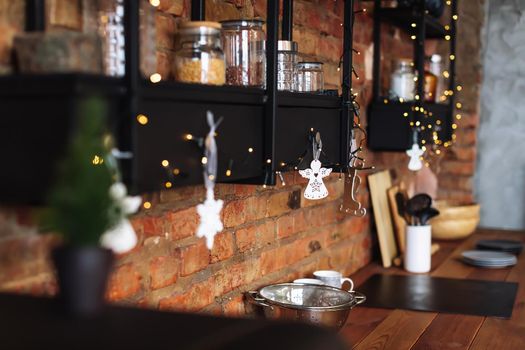 View of cozy decorated kitchen with wooden furniture. Stylish loft interior of studio with many lights. Concept of preparing Christmas Eve and New Year party.