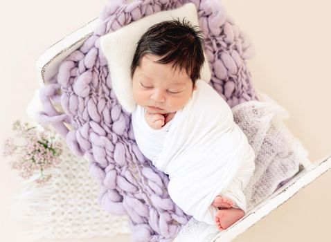 Funny newborn resting on tiny bed with pillow, top view