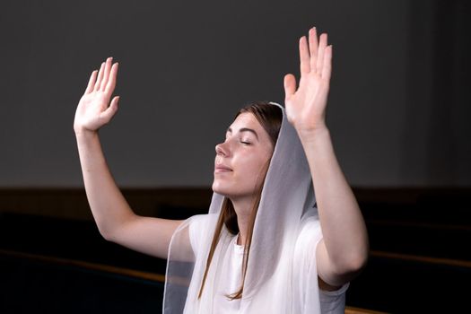 A young modest girl with a handkerchief on her head is sitting in church and praying. The concept of religion, prayer, worship.