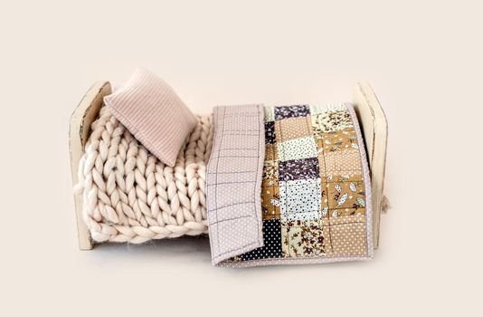 Wooden stylized small furniture bed with knitted pillow and handmade crafted blanket for newborn photoshoot in beige colors. Designed decoration object for infant studio photo