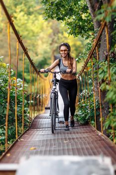 Attractive fit young woman wearing sportswear with her bicycle on suspension bridge at autumn