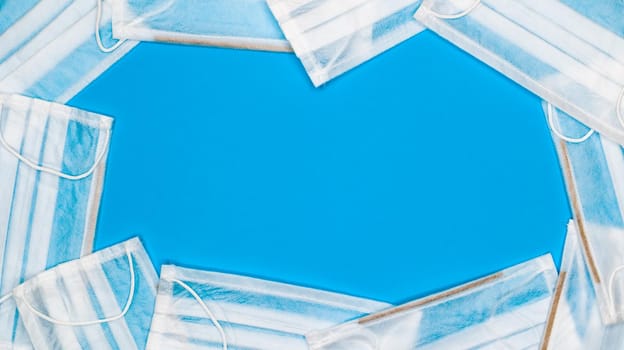 Many antiviral protective medical face masks with earloops are set against a blue background. Surgical mask background. Respiratory syndrome, coronavirus disease COVID-19. Copy space.