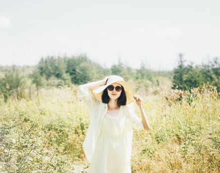 Summer stylish young woman in hat and sunglasses walking on sunny day outdoor.